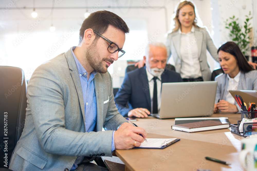 Handsome young business man writing notes on a clipboard in office