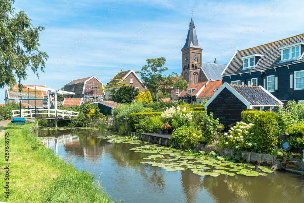 Marken, North Holland / Netherlands - June 23rd, 2019: Skyline of the old town with the bell tower and a traditional bridge over the canal