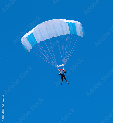 Skydiver with a white and blue parachute on a blue sky background.