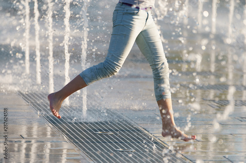 Photography of barefoot girls' legs jumping over the fountain.  Image with defocued background. Concepts of walking, happiness, childhood and freshness in hot summer day. photo