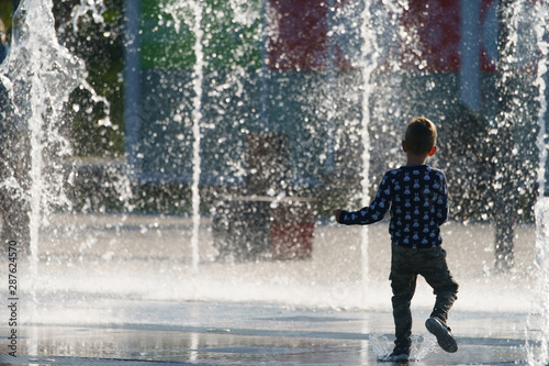 Photography of small boy playing with fountain. He running on water. Concepts of walking, happiness, childhood and freshness in hot summer day.