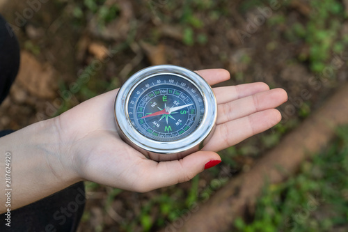Close up of young girl hand holding a vintage chinese compass in park with grass in background on sunny summer day. Travel, adventure, freedom, technology, trekking, map and orientation concept.