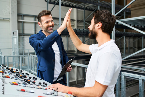 Happy businessman and employee high fiving at control panel in a factory photo