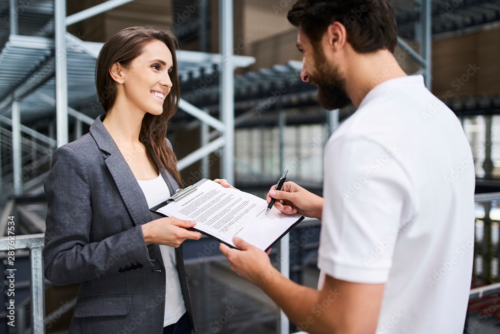 Man signing document in factory held by businesswoman Man signing document in factory held by businesswoman