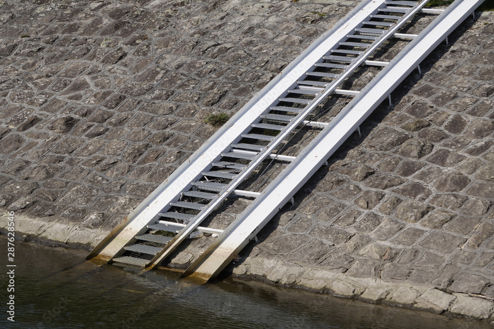 Obraz premium old iron ladder on the stone shore of the lake to lift a boat or boat ashore. traces of the level of movement of water in the lake
