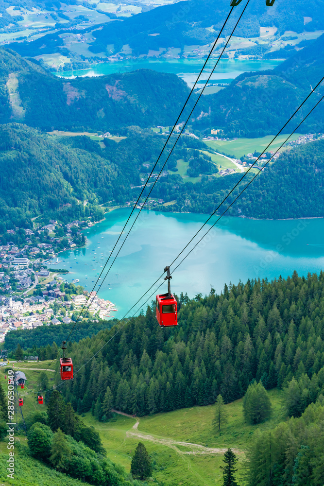 View of St.Gilgen village, Wolfgangsee lake and red Seilbahn cable car gondolas from Zwolferhorn mountain in Salzkammergut region, Austria - obrazy, fototapety, plakaty 