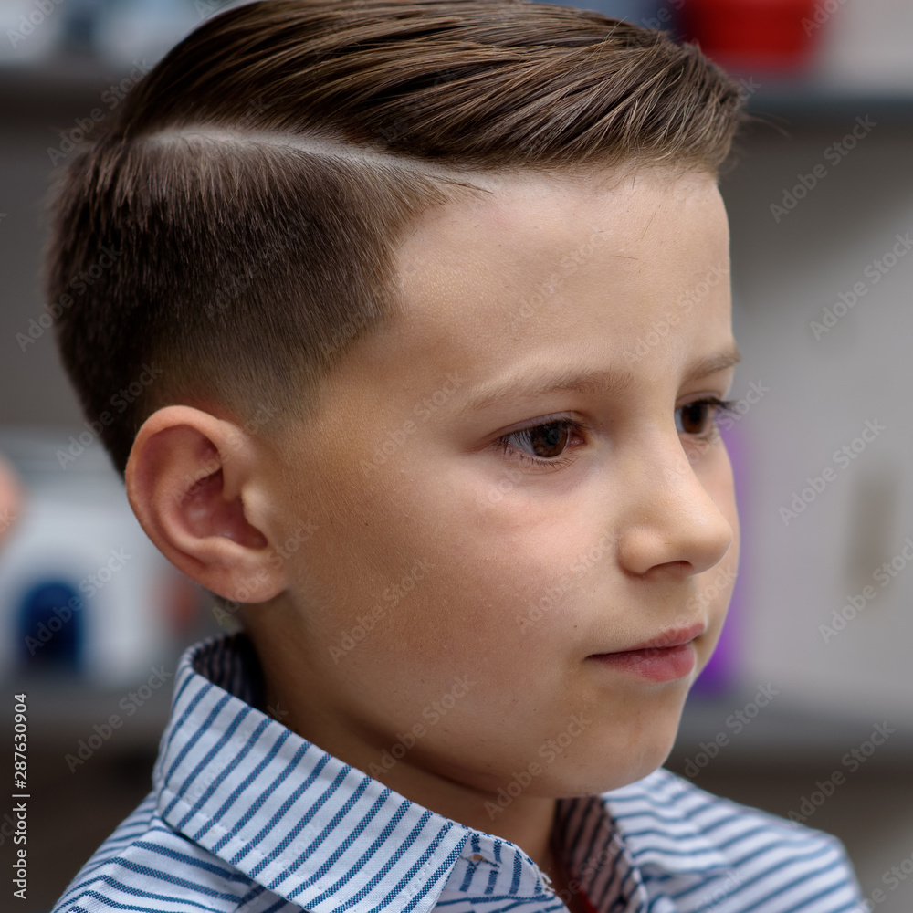 Barber shop. Boy with a totally new look is looking to himself at the mirror.. Barber shop. Boy with a totally new look is looking to himself at the mirror..