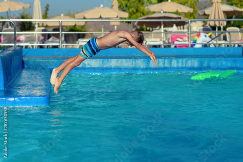 Portrait of Caucasian boy spending time in pool at resort during his summer vacations. He is jumping in to the water.