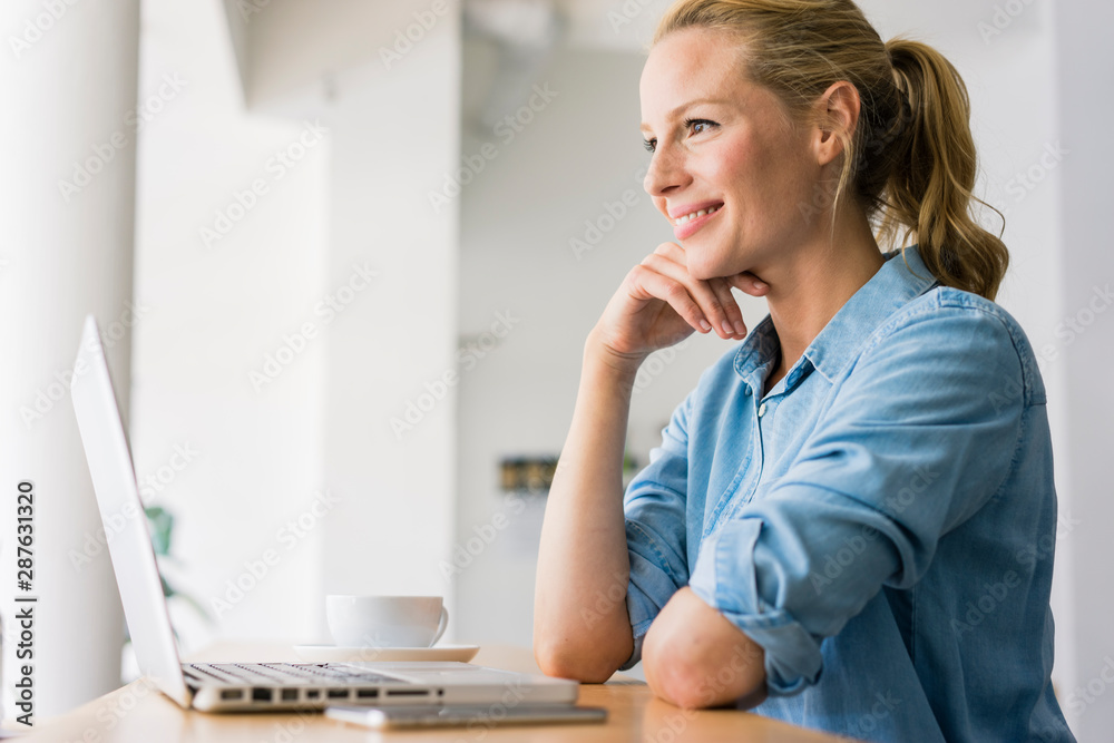 Blond woman sitting in coffee shop, using laptop Blond woman sitting in coffee shop, using laptop