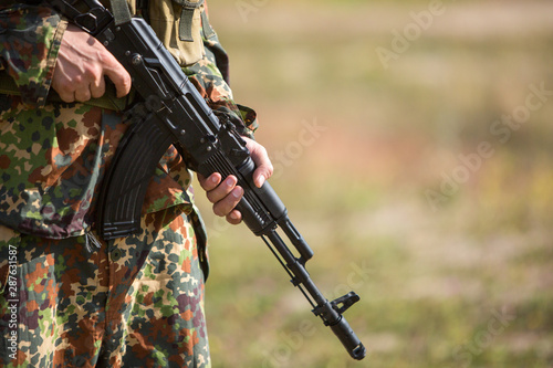 Soldier holds a rifle in his hands, close-up. A man in camouflage on the battlefield with a black machine gun