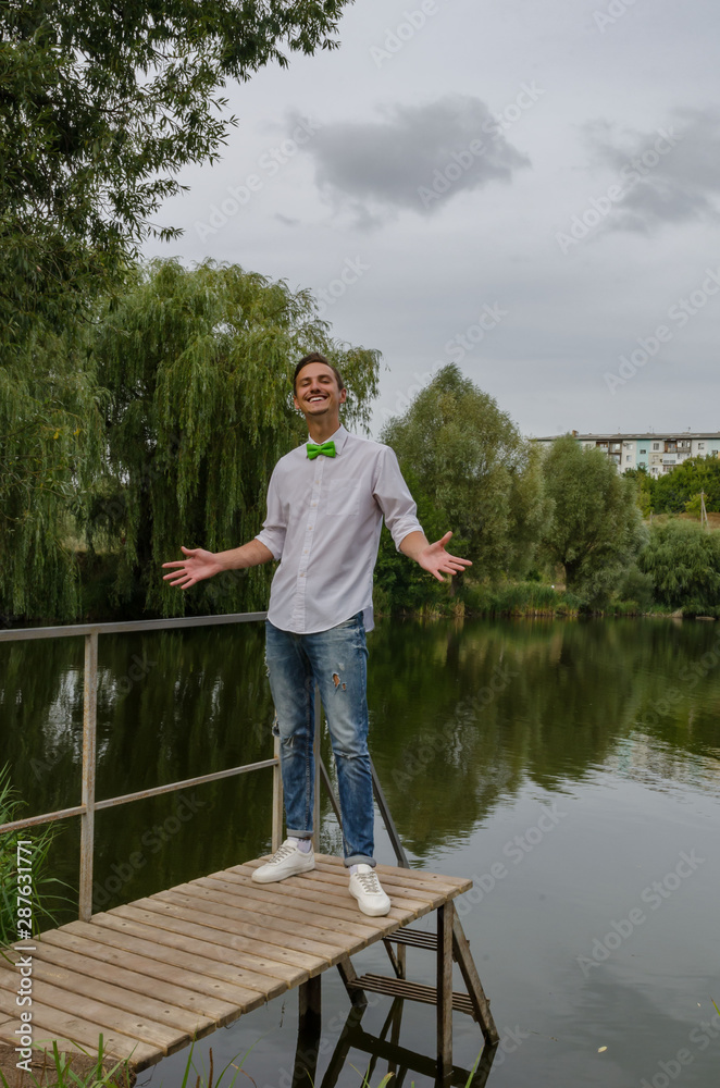 young man with a green bow-tie on a bridge on a lake background young man with a green bow-tie on a bridge on a lake background