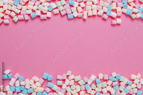 Frame made of white and pink sweet marshmallow candys with copy space on a pink background.