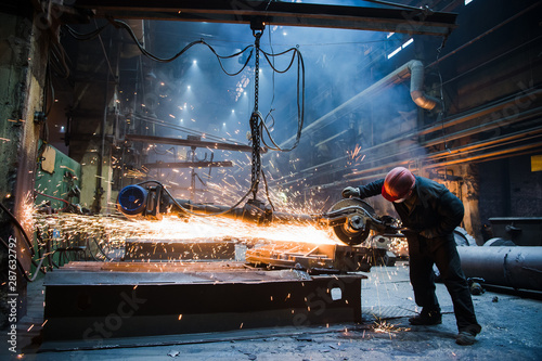 Employee grinding steel with sparks - focus on grinder. Steel factory. photo