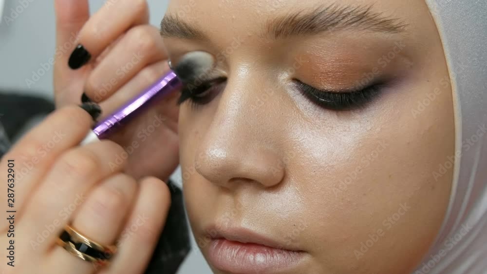 Woman make-up artist stylist makes makeup fashionable pink smoky eyes with special makeup brush of a young model Woman make-up artist stylist makes makeup fashionable pink smoky eyes with special makeup brush of a young model
