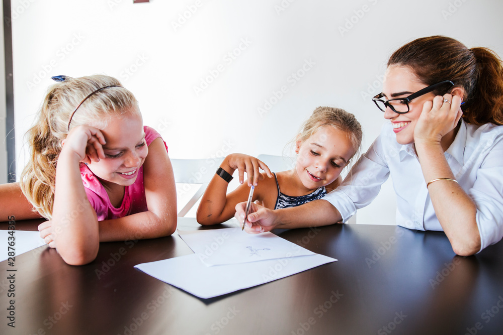 Happy teacher sitting at desk with two schoolgirls writing on paper Happy teacher sitting at desk with two schoolgirls writing on paper