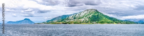 Panorama of clouds above Angarsnesvika marina, fjord and mountains. Tides out but green and brown seagrass remains on the coast of Alsta Island. Close to Sandnessoen town, Norway