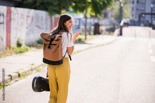 Young woman carrying violin case using cell phone on the street
