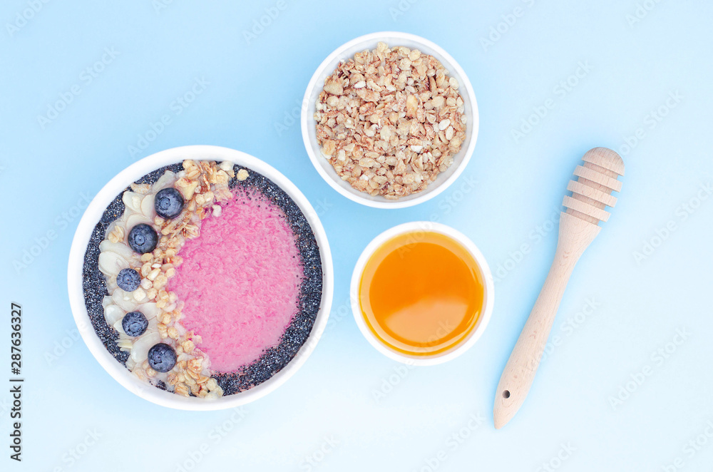 Smoothie bowl with fruits and granola and honey on a blue background.