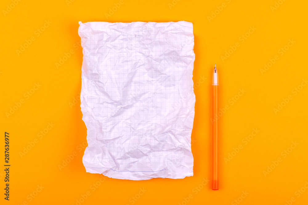 White crumpled sheet of paper with a notebook for texts, notes and drawings next to a yellow pen lies on an orange background