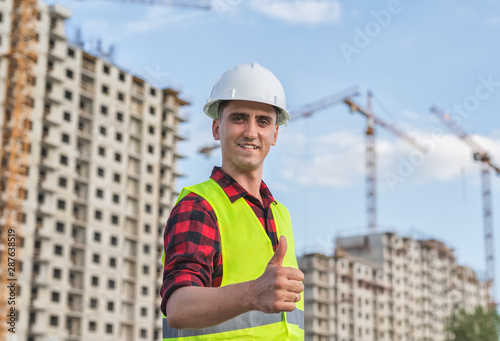 civil engineer in a white helmet on the background of construction, with a raised thumb.