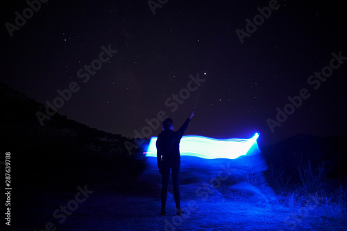 Human silhouette against blue backlight against night starry sky. Light painting photography. Long exposure.