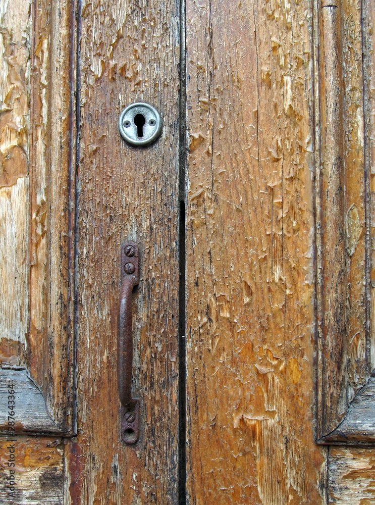 close up of an old brown varnished peeling wooden door with keyhole and rusty handle close up of an old brown varnished peeling wooden door with keyhole and rusty handle