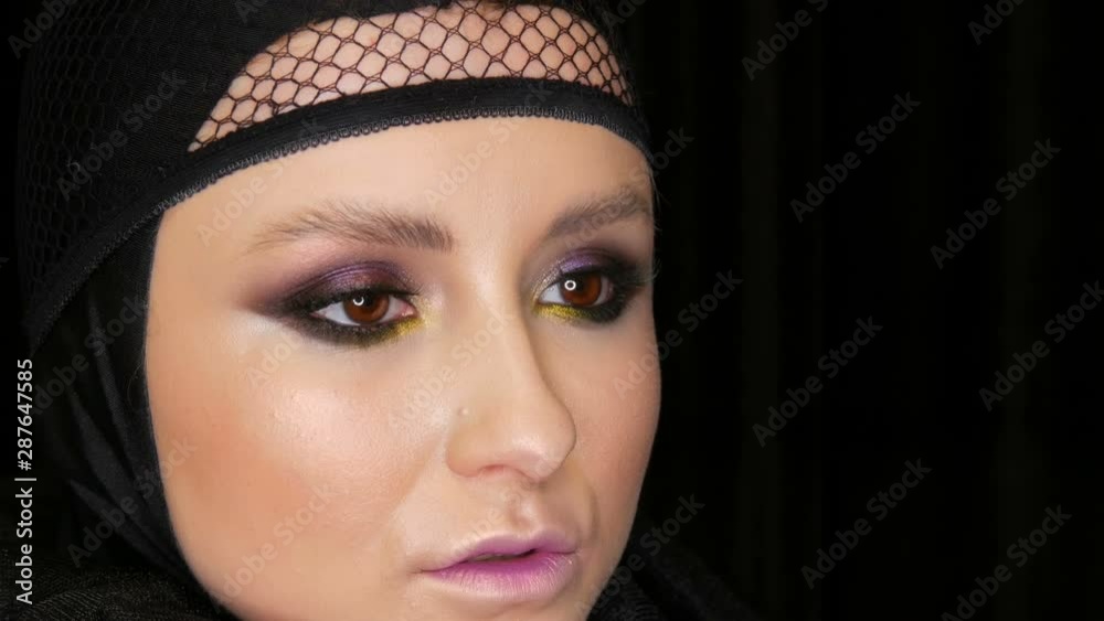 Professional girl model with beautiful makeup poses in a black cap on her head in front of the camera on a black background in the image of a black widow. High-fashion Professional girl model with beautiful makeup poses in a black cap on her head in front of the camera on a black background in the image of a black widow. High-fashion