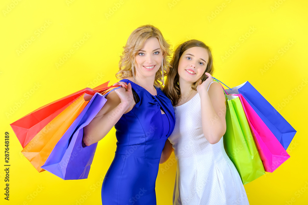 Cute blonde girl with her daughter holds shopping bags in her hands, looks at the camera and smiles