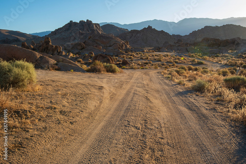 dirt road in desert landscape with rocky hills and distant Sierra Nevada mountains