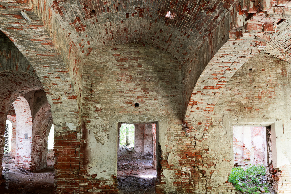 Old dilapidated red brick building. The room inside with vaults of crumbling brick. Wide walls, large openings of windows and doors.