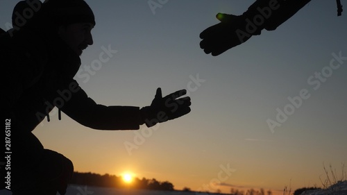 teamwork desire to win. close-up. Climbers help friend climb stretch of helping hand. Silhouette of travelers in winter on hill in bright rays of sun. sports tourism concept.