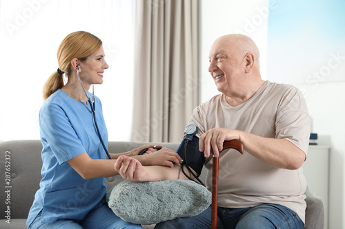 Nurse measuring blood pressure of elderly man indoors. Assisting senior people