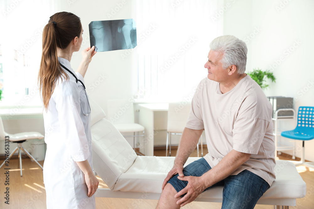 Obraz premium Young doctor with X-ray and senior patient in clinic. Knee problem