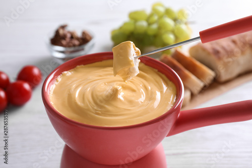 Dipping bread into pot with cheese fondue on table  closeup
