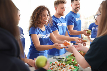 Volunteers serving food to poor people indoors