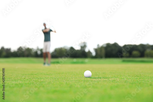 Man playing golf on green course, ball in focus. Sport and leisure