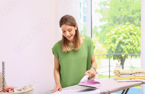 Young pretty woman ironing clean laundry indoors