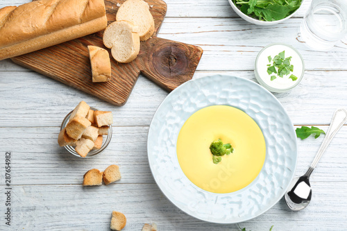 Bowl of cheese cream soup with broccoli served on white wooden table, flat lay