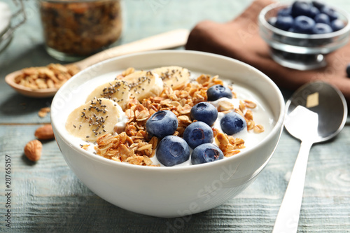 Foto Bowl of yogurt with blueberries, banana and oatmeal on color wooden table