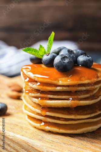 Wooden board with pancakes, syrup and blueberries on table, closeup