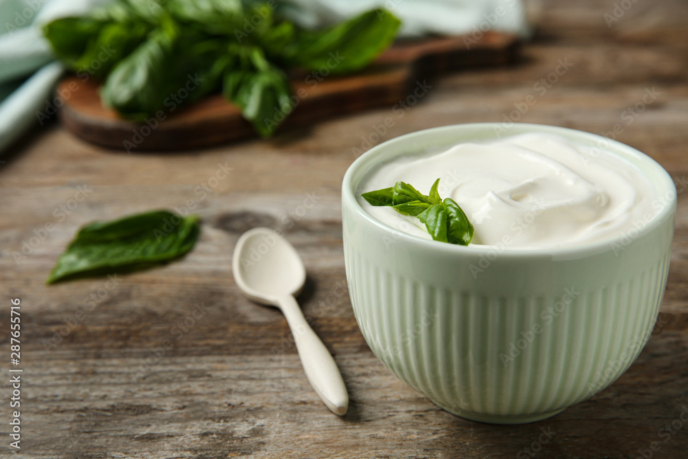 Bowl of fresh sour cream with basil and spoon on wooden table. Space for text Bowl of fresh sour cream with basil and spoon on wooden table. Space for text