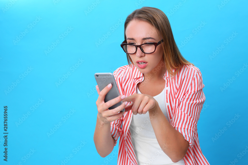 Young woman with glasses using mobile phone on blue background. Vision problem Young woman with glasses using mobile phone on blue background. Vision problem