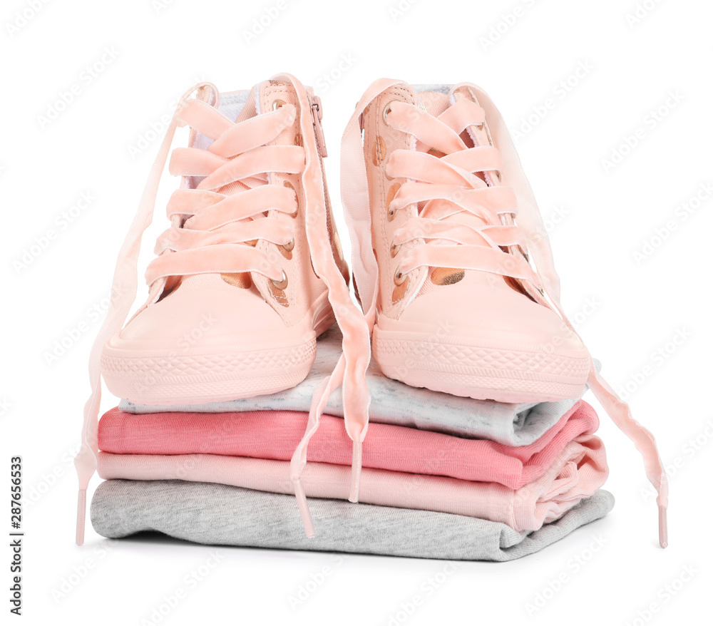 Stylish child shoes and stack of clothes on white background