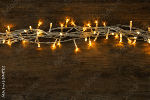 Glowing Christmas lights on wooden background, top view. Space for text