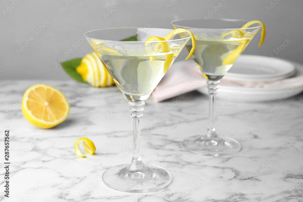Glasses of lemon drop martini cocktail with zest on marble table against grey background