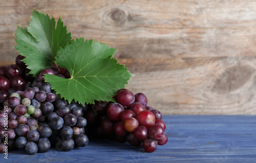 Fresh ripe juicy grapes on blue table against wooden background. Space for text