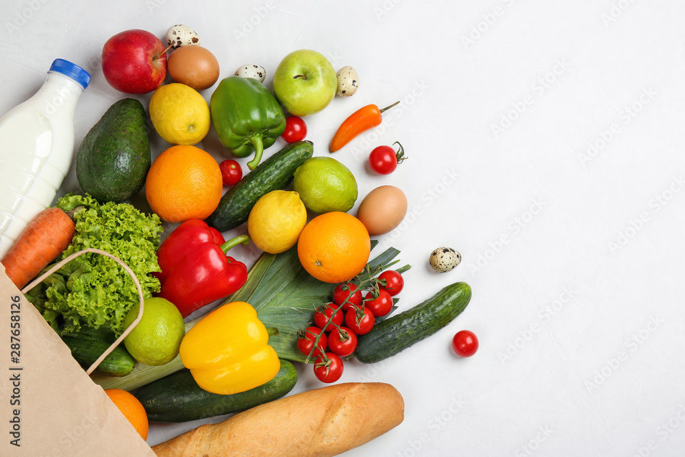 Flat lay composition with overturned paper bag and groceries on white table Flat lay composition with overturned paper bag and groceries on white table