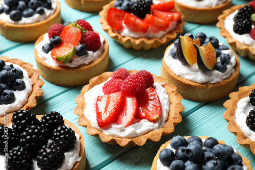Many different berry tarts on blue wooden table. Delicious pastries