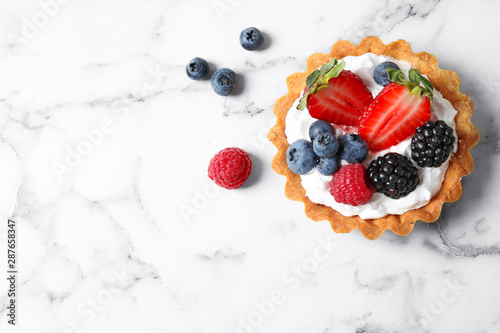 Top view of tart with different berries on marble table, space for text. Delicious pastries