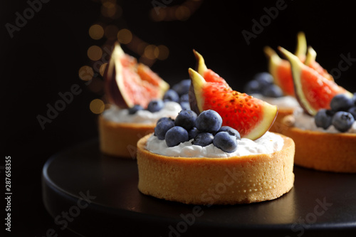 Valokuvatapetti Tarts with blueberries and figs on black table against dark background, closeup